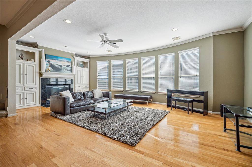 Living Room - 23 x 12: Open living area with soaring ceilings, gas-log fireplace with stone surround and decorative mantle, wood floors and wall-to-wall windows, bringing in abundant natural light. Plenty of storage cabinets with display cabinets. Wood floors, base boards with quarter round, crown molding and recessed lighting.
