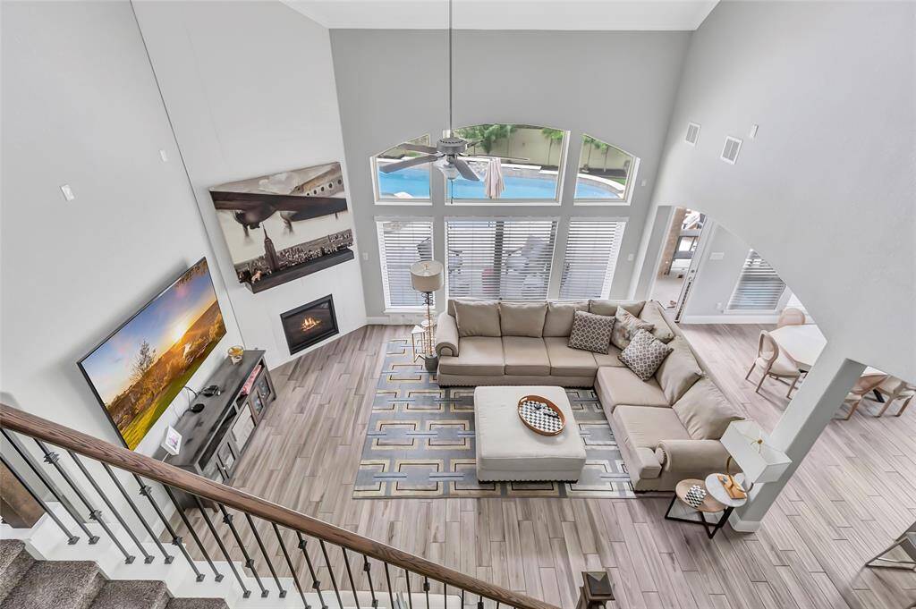 This spacious living room features high ceilings and abundant natural light from large windows overlooking a pool. It includes a cozy fireplace, and modern flooring.The open layout connects seamlessly to the dining area, creating an inviting and functional space for entertaining.