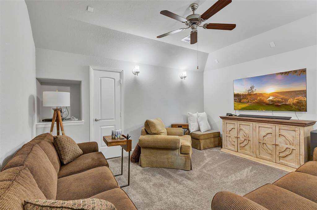 Cozy media room featuring  neutral colors, wall sconces for lighting, and a ceiling fan for comfort. Perfect for relaxation and entertainment.