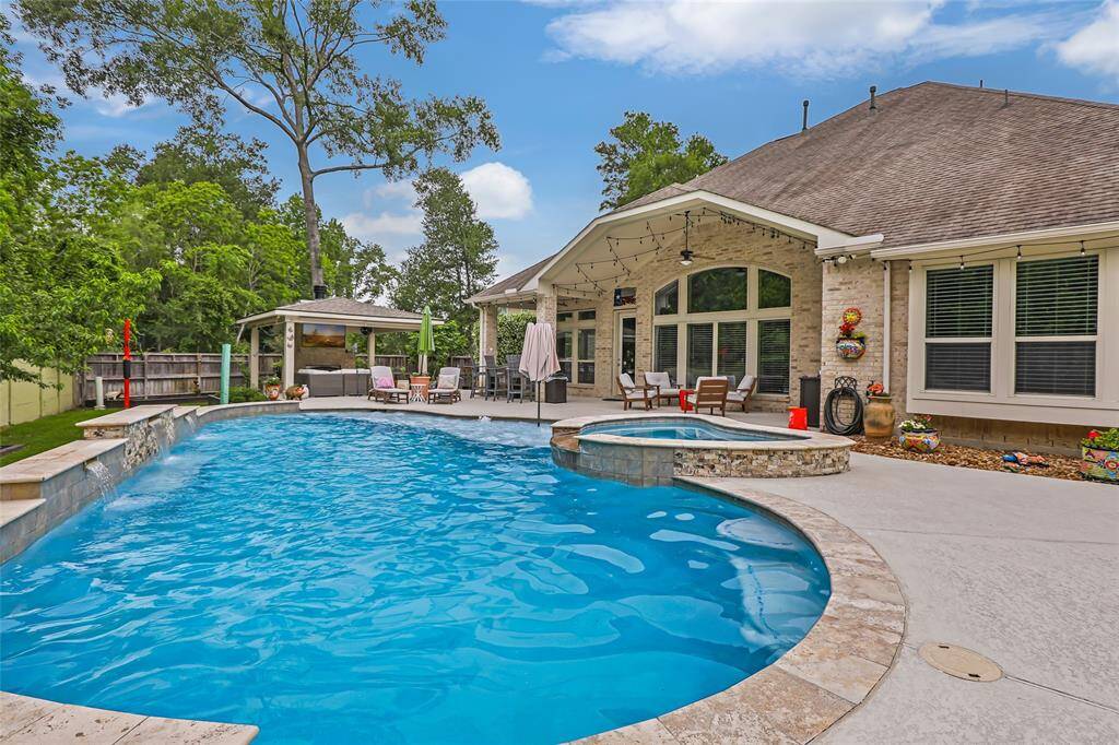 This photo showcases a spacious backyard with a large, inviting swimming pool and spa. It features a covered patio with comfortable seating, perfect for outdoor entertaining, surrounded by lush greenery for added privacy.