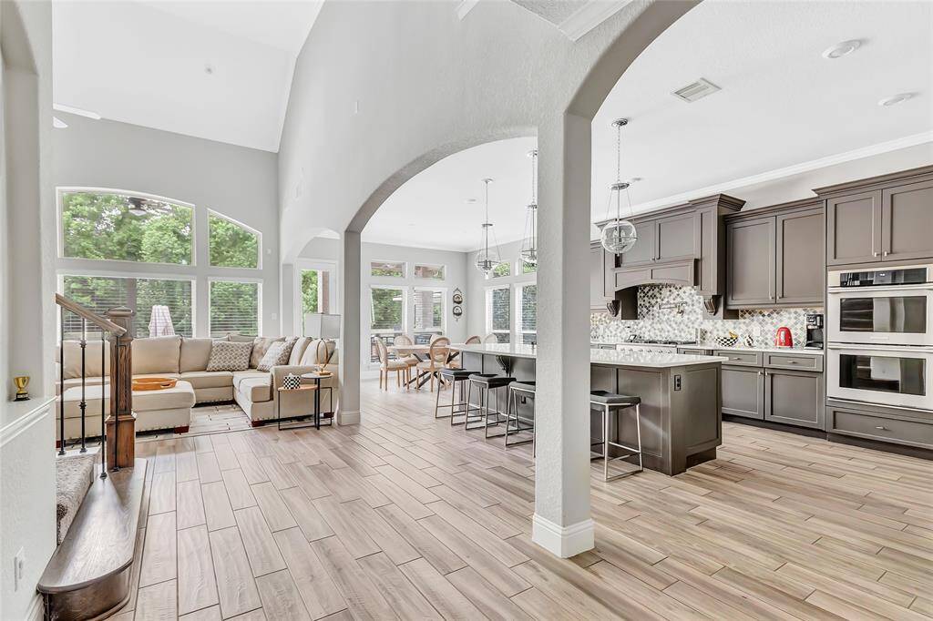 Spacious modern kitchen with sleek gray cabinetry, a large central island with quartz countertops, and stainless steel appliances. It features a stylish tile backsplash, pendant lighting, and ample storage, creating an inviting and functional cooking space.