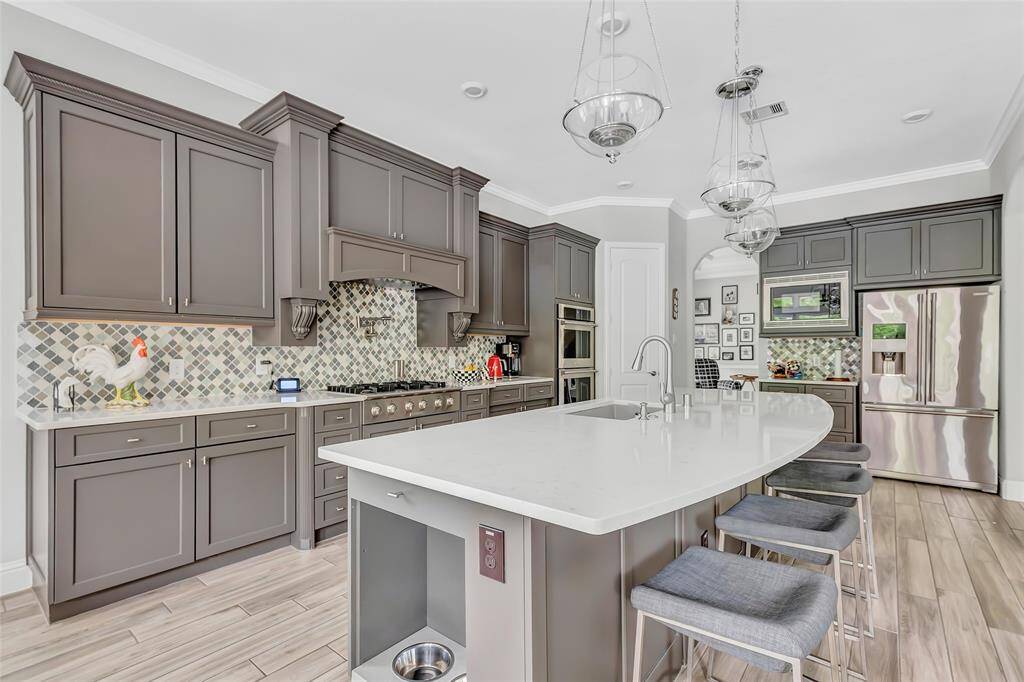 spacious white quartz island with built-in storage, and stainless steel appliances. The open layout includes stylish pendant lighting providing a warm and inviting atmosphere.