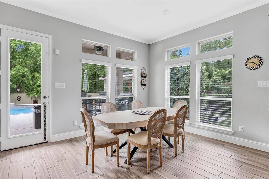 Bright dining area with large windows, wood-look tile flooring, and a view of the backyard and pool through glass doors. Ideal for enjoying natural light and outdoor access.