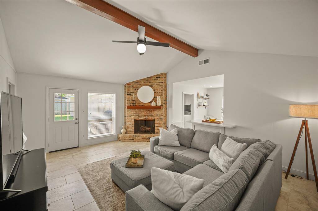 Family room has a vaulted ceiling with a wood beam accent, retro brick fireplace, and door to the patio and back yard.