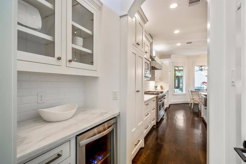 Sophisticated butler’s pantry with marble countertops, glass display cabinetry, and a built-in wine fridge provides stylish utility, perfectly positioned between the kitchen and dining areas, making entertaining a breeze.