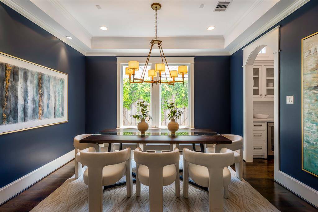 Wrapped in a moody yet inviting hue with layered ceiling details, the formal dining room makes a bold statement with elegant crown molding, natural light, and a modern brass chandelier, bringing a sense of intimacy and sophistication to the dining room.