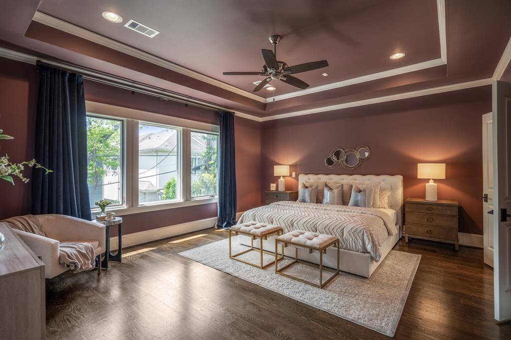The primary bedroom stuns with rich, moody walls, dramatic tray ceilings, and oversized windows that flood the room with natural light, equal parts luxurious and relaxing.
