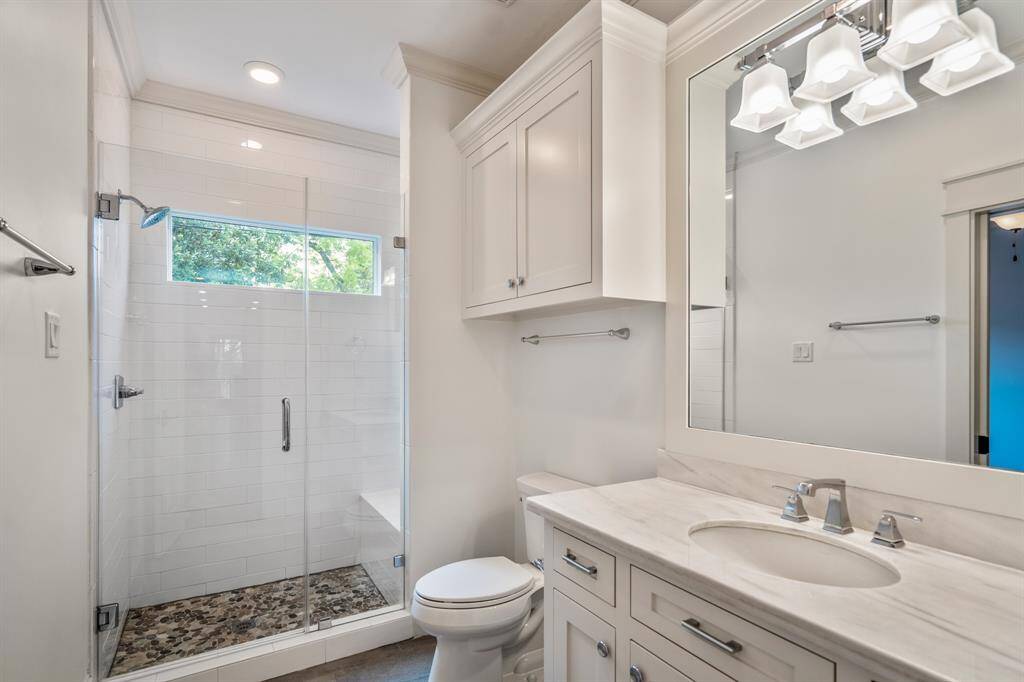 The private, ensuite full bathroom is finished with marble counters, polished chrome hardware, and a frameless glass shower that keeps the space feeling bright and airy.