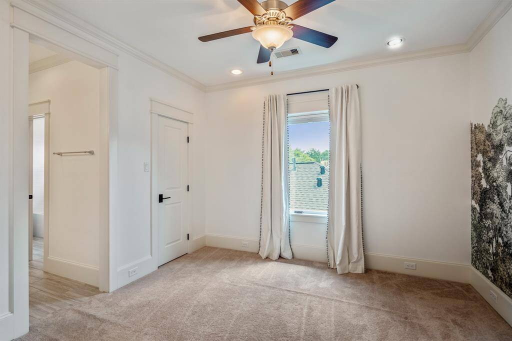 This secondary bedroom offers plush carpet, crown molding, and an ensuite layout with a walk-in closet, perfect for a nursery, guest room, or personalized children’s space.