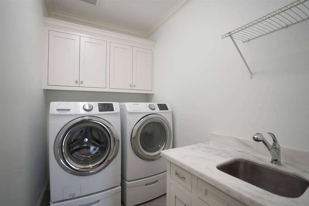 The utility room is complete with built-in storage, a handy sink, and sleek front-loading machines to make laundry day a little more luxe.