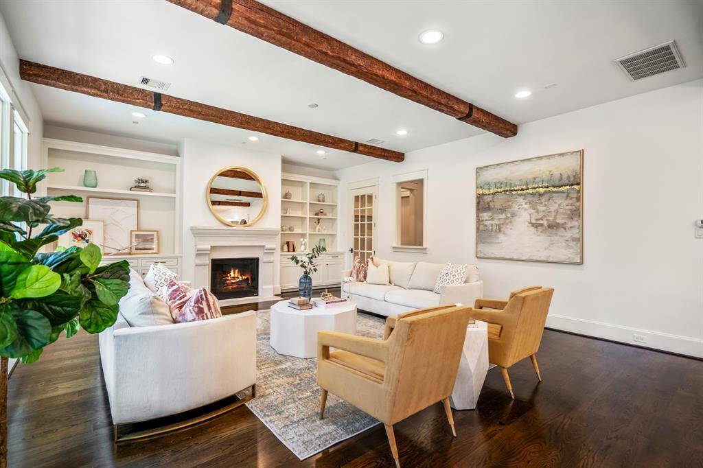 The living room exudes relaxed elegance with exposed wood beams, custom built-ins, and a stone fireplace that anchors the space in warmth and character. Just beyond the window-paned door, the family room discreetly merges with the mudroom, garage, and a charming wet bar - maintaining style and function in everyday transitions.
