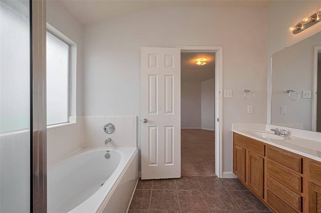 Primary bathroom features has a large vanity with ample storage, and neutral tile flooring. A frosted window provides natural light while maintaining privacy.