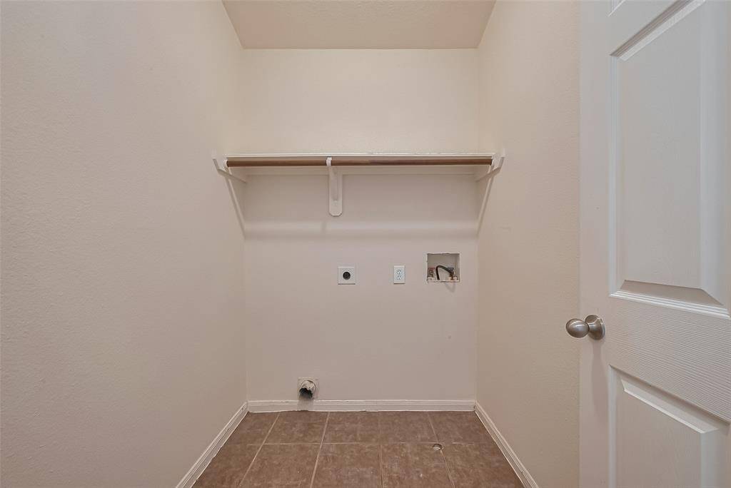 This photo shows a compact laundry room with hookups for a washer and dryer, a shelf for storage, and tiled flooring.