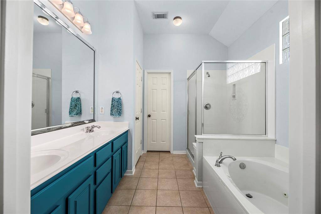 Bathroom features a double vanity, cabinetry, a spacious glass-enclosed shower, and a separate tub.