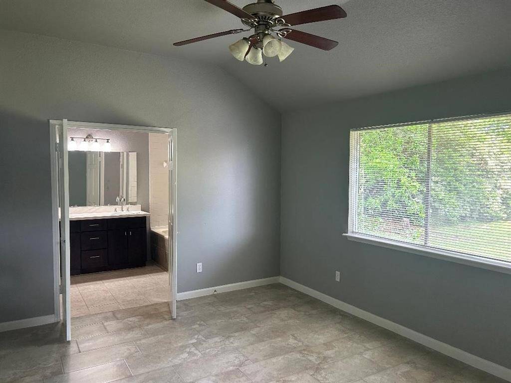 This bright Master bedroom features a large window with garden views, a ceiling fan, and connects to a bathroom with dual sinks and modern fixtures.