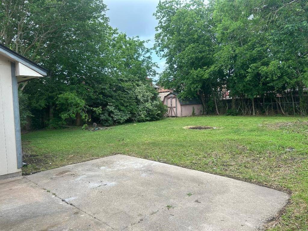 Spacious backyard with a concrete patio, lush green lawn, mature trees for privacy, and a storage shed, ideal for outdoor activities and gardening.