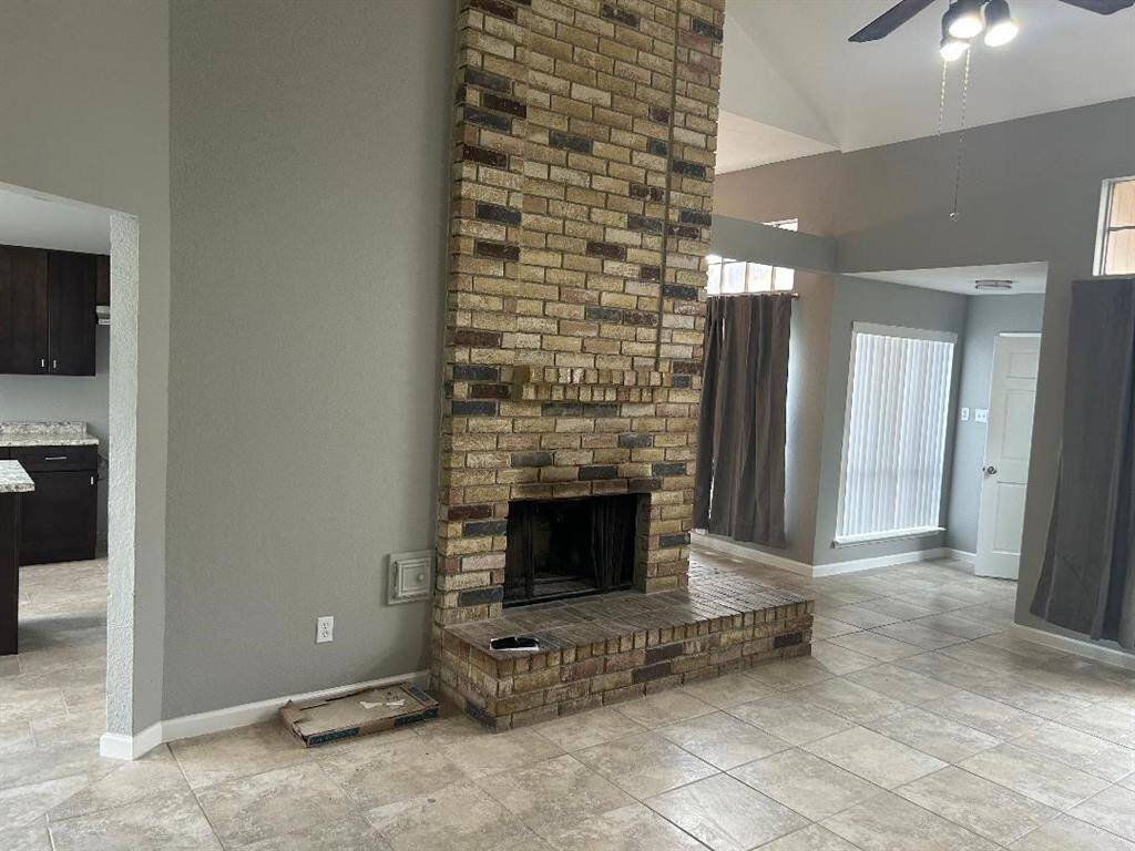 Living area features a striking floor-to-ceiling brick fireplace, high ceilings and large windows for natural light. View into the kitchen area on left.