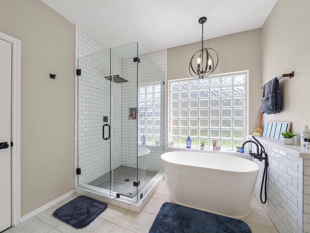 Indulge in the ultimate relaxation in this exquisitely appointed bathroom. Featuring a luxurious freestanding tub accentuated by a contemporary light fixture, this space offers a serene and spa-like retreat. The glazed block window provides natural light while maintaining privacy. A separate, fully tiled frameless shower completes this sophisticated and functional design