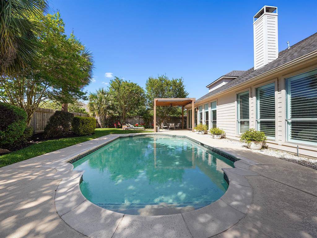 The inviting pool is surrounded by mature trees and lush landscaping, creating a serene and tranquil environment.