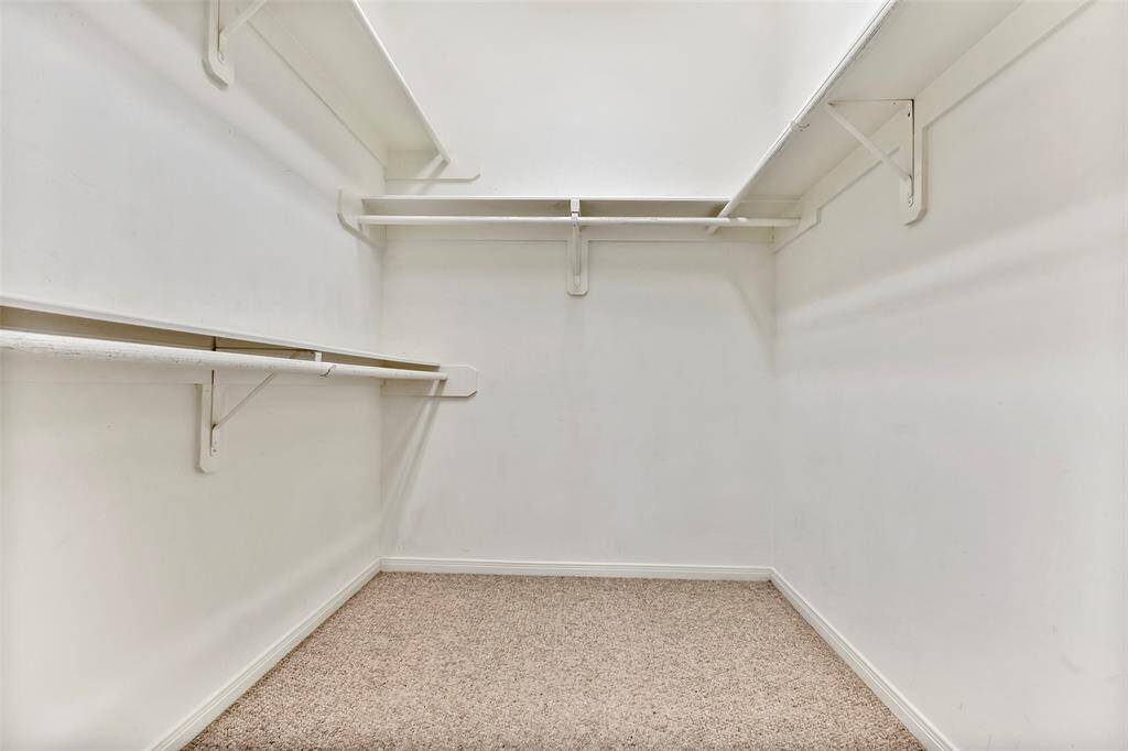 Spacious walk-in closet with carpeted floors, ample shelving, and a full hanging rod for all your storage needs.