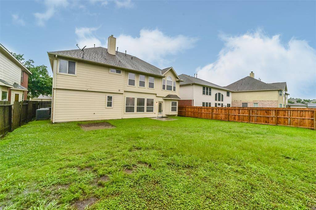 This photo shows the spacious backyard of a two-story house with a large lawn and a wooden fence. The exterior is light-colored, with several windows offering ample natural light. Ideal for outdoor activities or future landscaping.