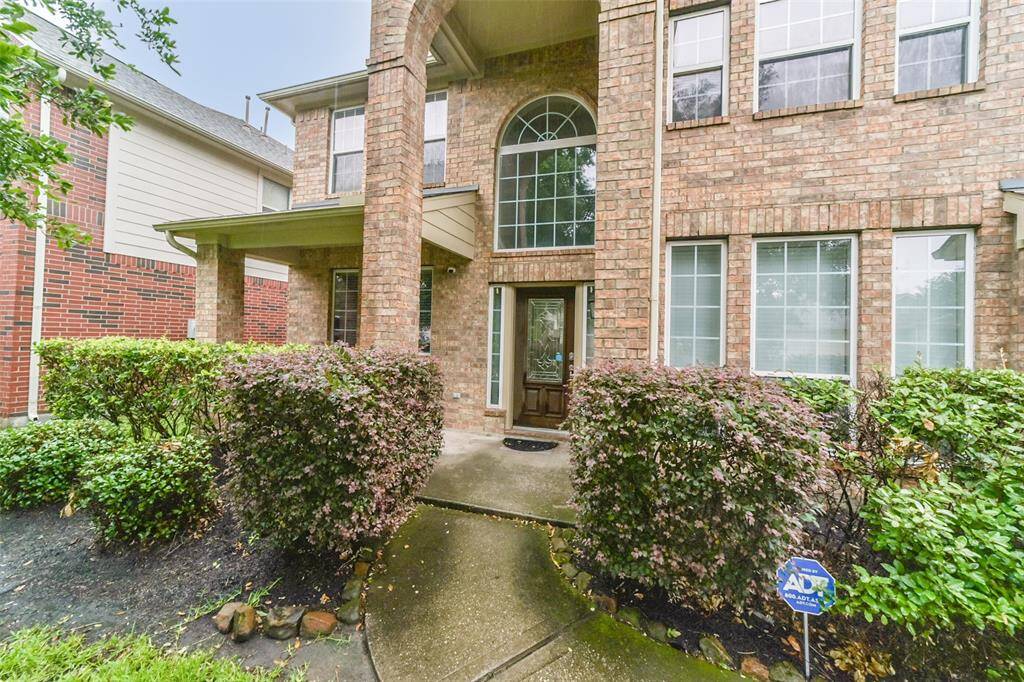 This charming two-story brick home features a welcoming front entrance with large windows, an arched transom, and a covered porch. Surrounded by well-maintained shrubs, it offers both privacy and curb appeal.
