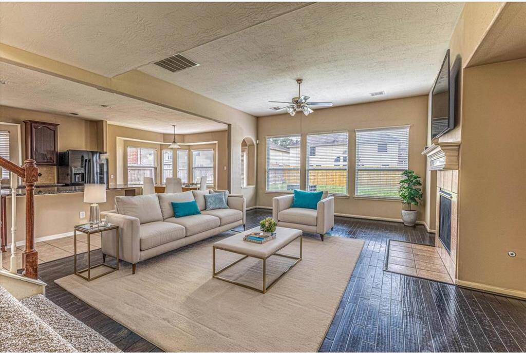 This inviting living area features an open layout with a cozy fireplace, elegant hardwood floors, and abundant natural light from large windows. The adjacent kitchen and dining space enhance the home's modern feel, perfect for entertaining.
