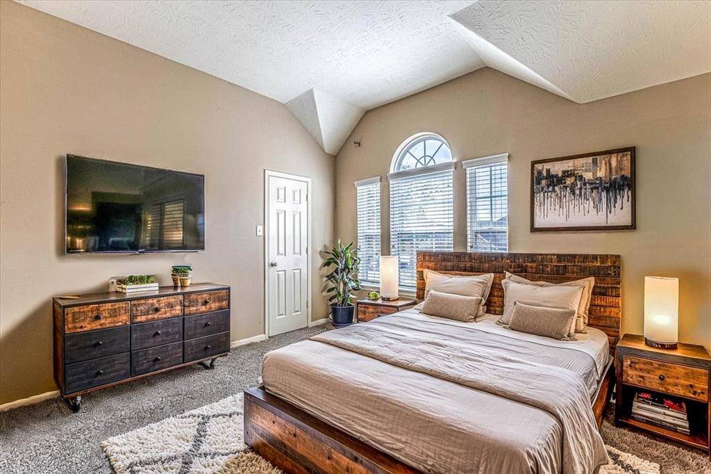 This bedroom is spacious and well-lit, featuring a vaulted ceiling and large arched windows. Neutral tones and plush carpeting add warmth.