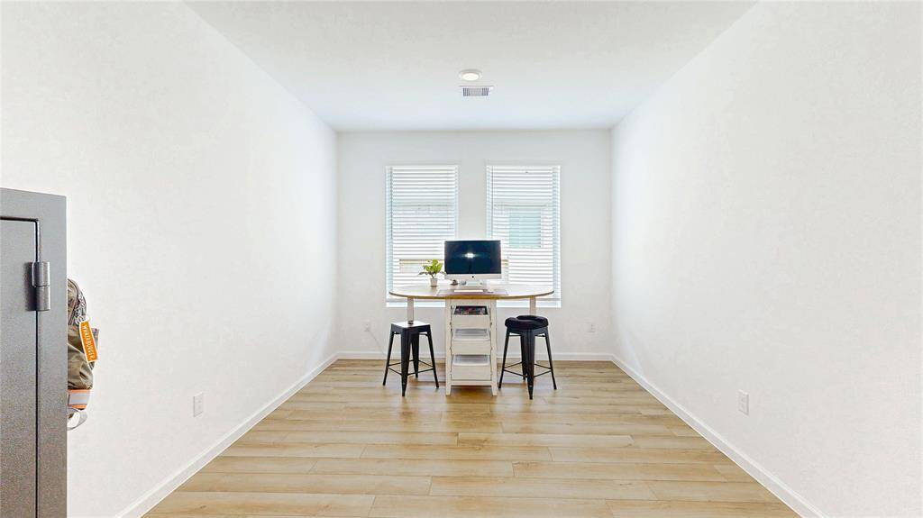 Bright, minimalist home office with vinyl plank flooring and natural light from two windows, creating a functional and airy workspace.