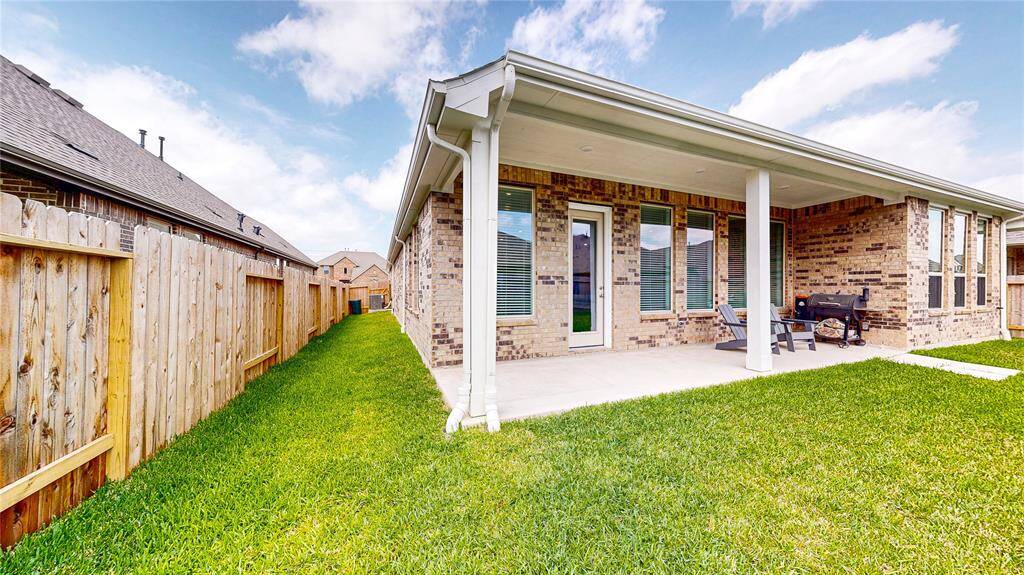This photo showcases a backyard with a well-maintained lawn and a brick house featuring a covered patio area. The space provides ample room for outdoor seating and activities, offering privacy with a wooden fence. Ideal for relaxation and entertaining.
