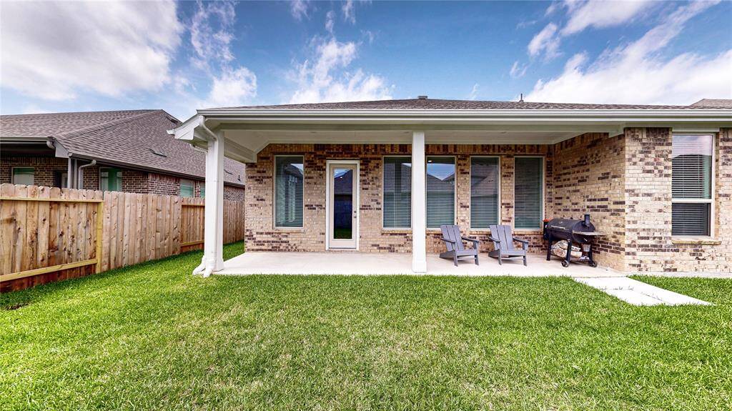 This photo features a cozy backyard with a covered patio, perfect for relaxation. The brick exterior adds charm, while the lawn offers space for outdoor activities. Ideal for enjoying outdoor meals or quiet mornings.