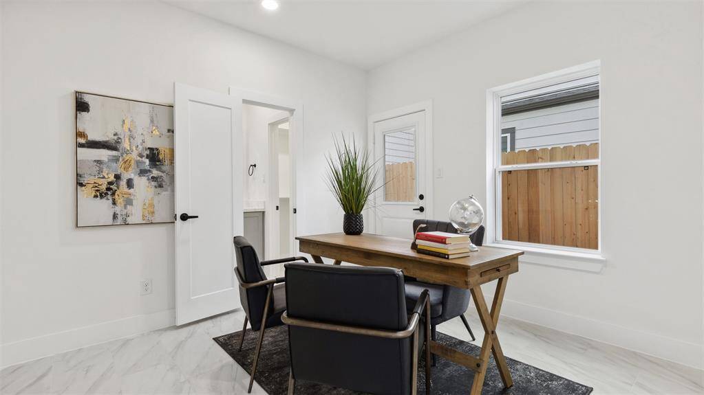 Modern, bright office space highlighted with clean lines, a large window for natural light, recessed lighting and sleek, marble-like tile flooring.