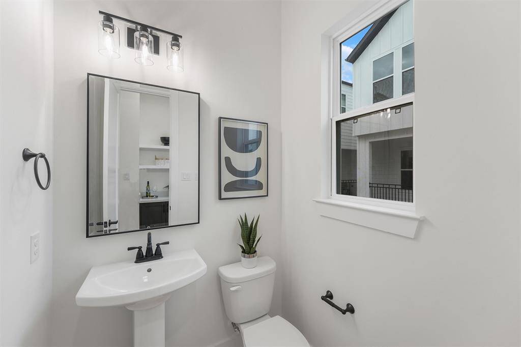 Your modern half-bathroom comes completed with custom paint, featuring a pedestal sink, and a modern framed black matte mirror with overhead lighting. A window allows for rays natural lighting.