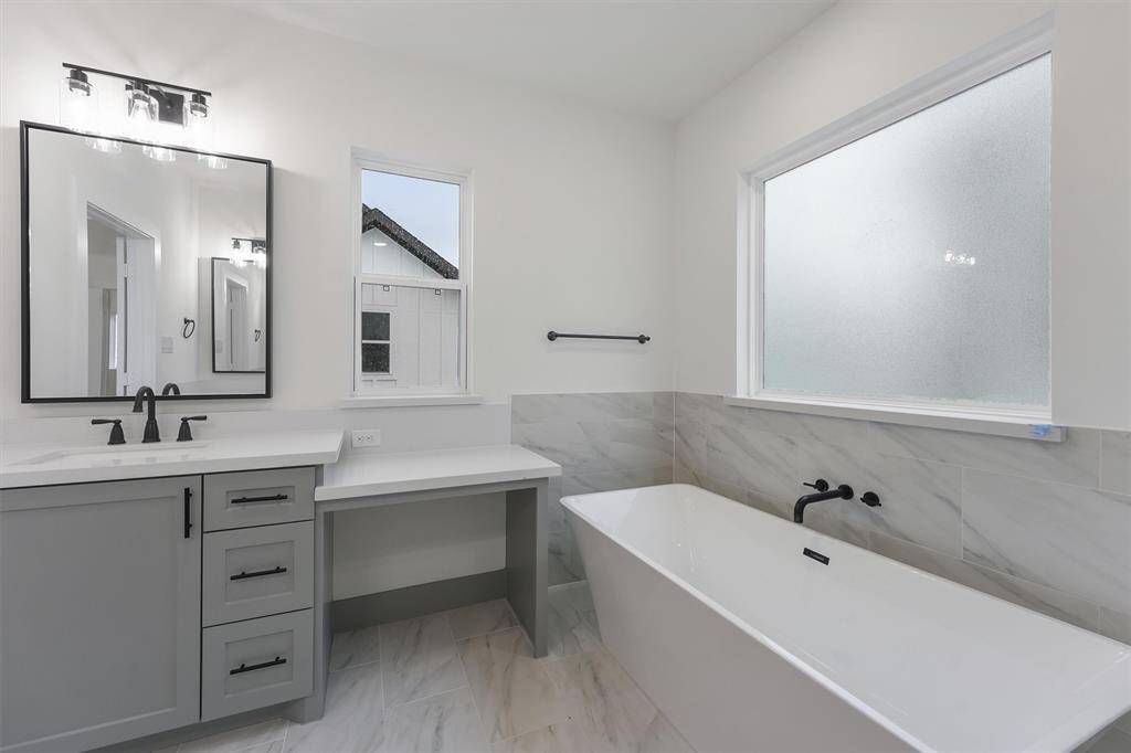 This is a modern primary bathroom featuring a double vanity with framed black matted mirrors, ample storage space and a spacious bathtub with a marble surround. The room is well-lit, with a frosted window ensuring privacy. This kitchen set up is in Plan A only.