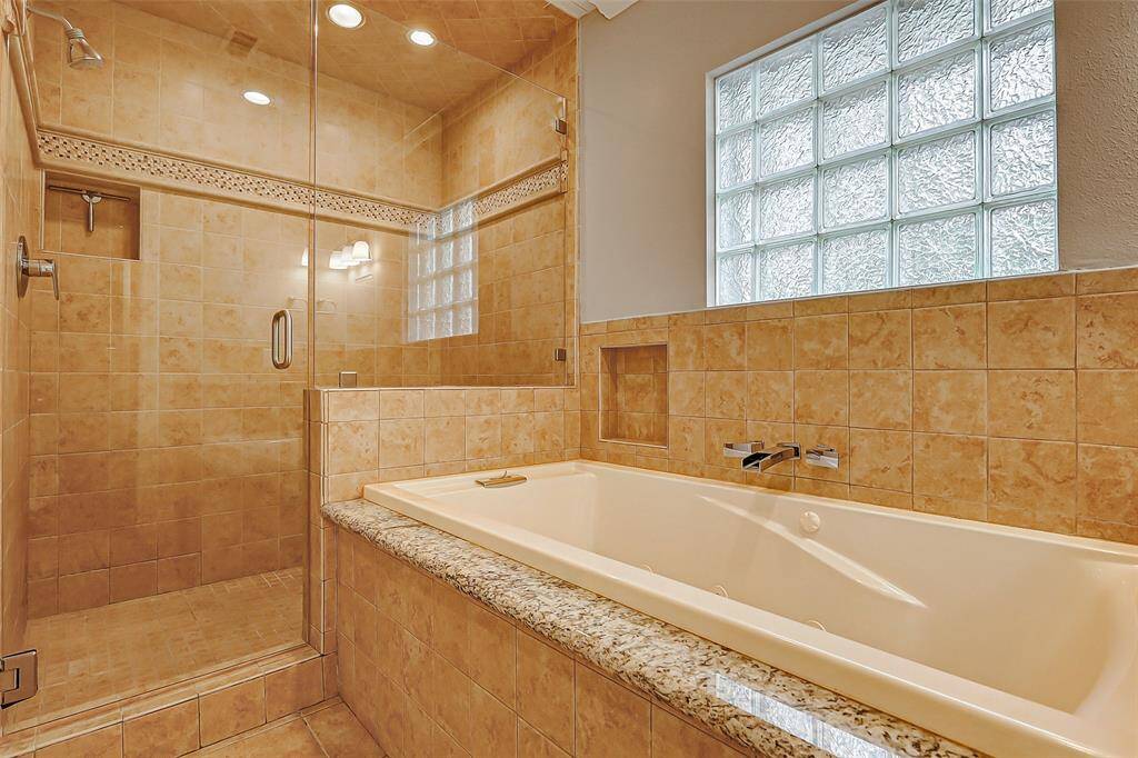The jetted tub is perfectly positioned beneath an obscure window, allowing natural light to fill the space while maintaining privacy. The wall-mounted faucet adds a sleek, spa-like touch to this tranquil retreat.