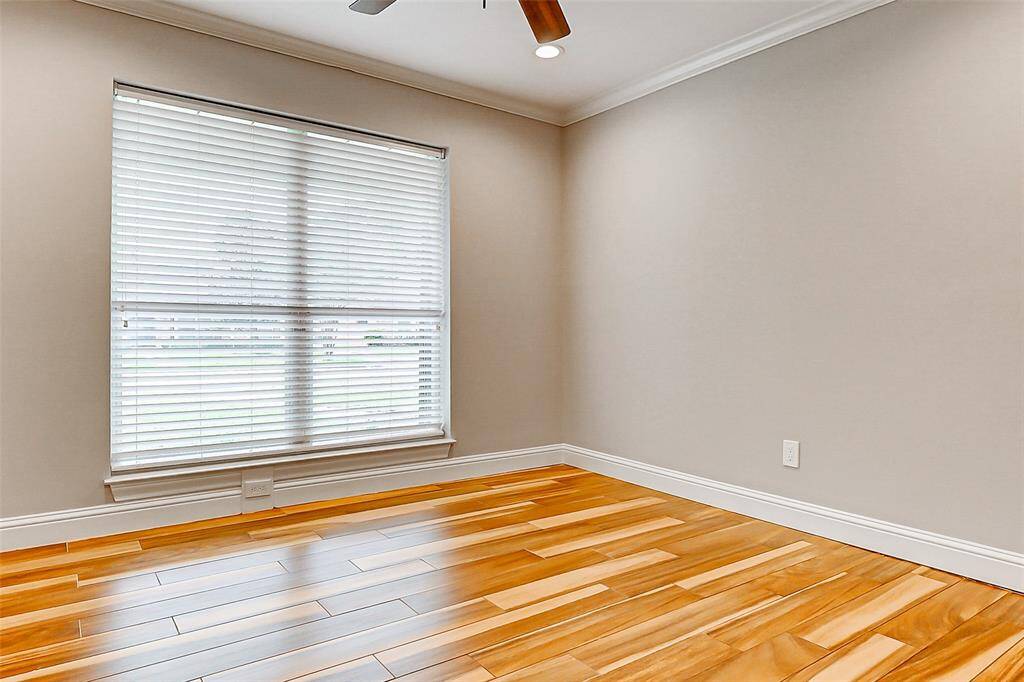 This charming home also includes three additional guest bedrooms. This particular room features wood-look tile floors, crown molding, a ceiling fan, and a large floor-to-ceiling window, filling the space with natural light.
