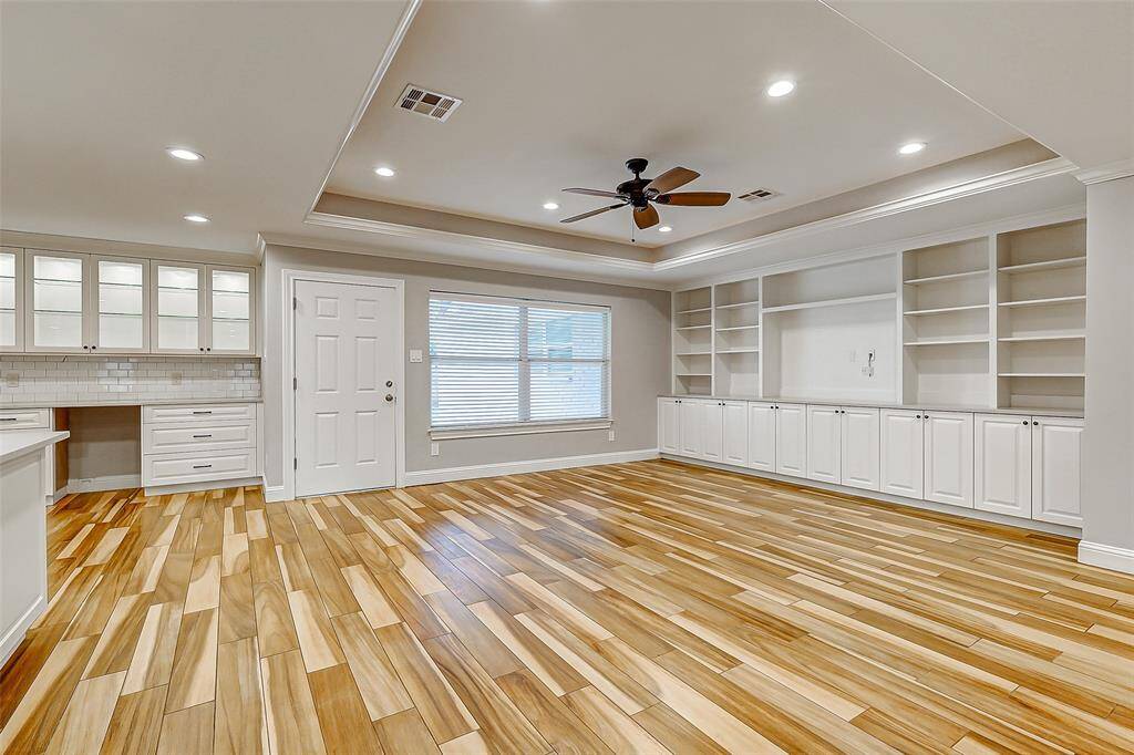Welcome to your expansive living area, where a tray ceiling with recessed lighting and a ceiling fan immediately captures the eye. The room also boasts decorator paint, wood-look tile floors, custom built-ins, and a large window that offers views of the backyard.
