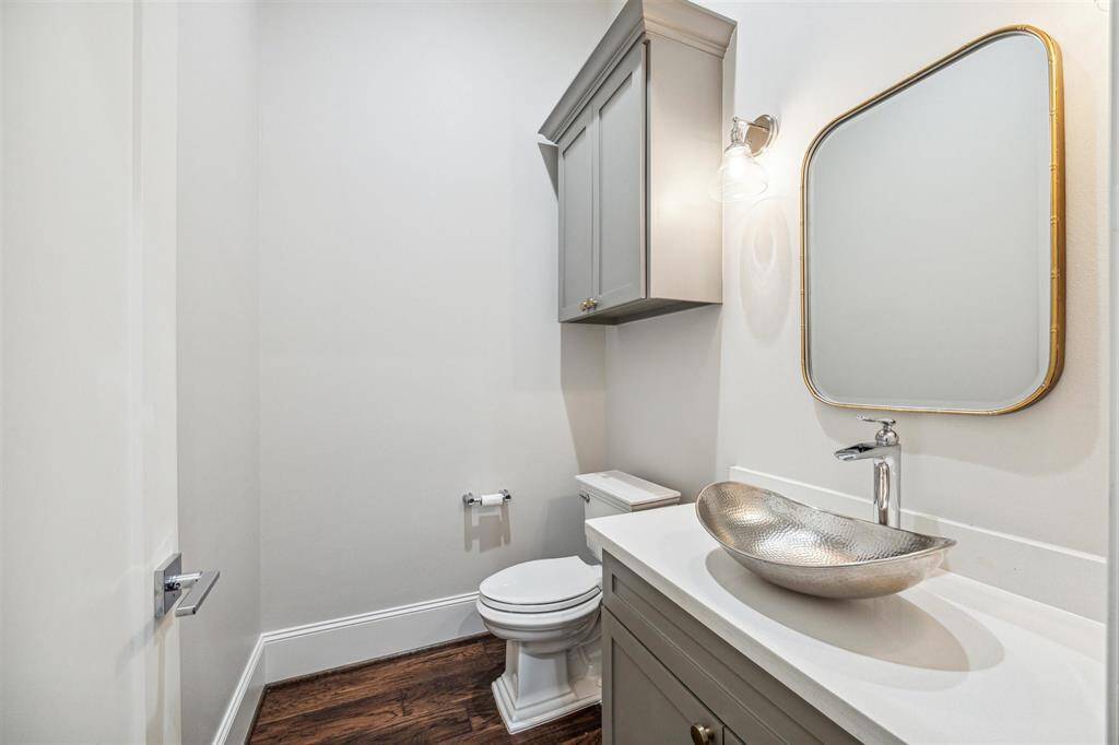 The chic powder room showcases a hammered metal vessel sink, porcelain countertops, custom cabinetry, and a brushed gold-framed mirror.