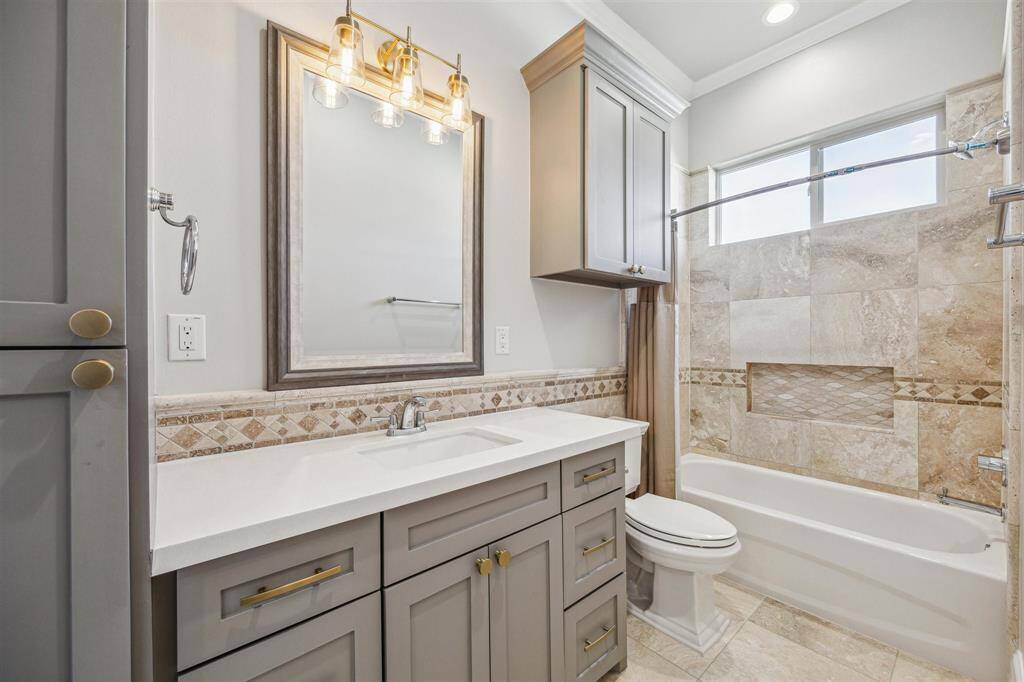 Secondary bathroom with ample built-in storage, tiled tub surround, framed mirror and designer lighting.