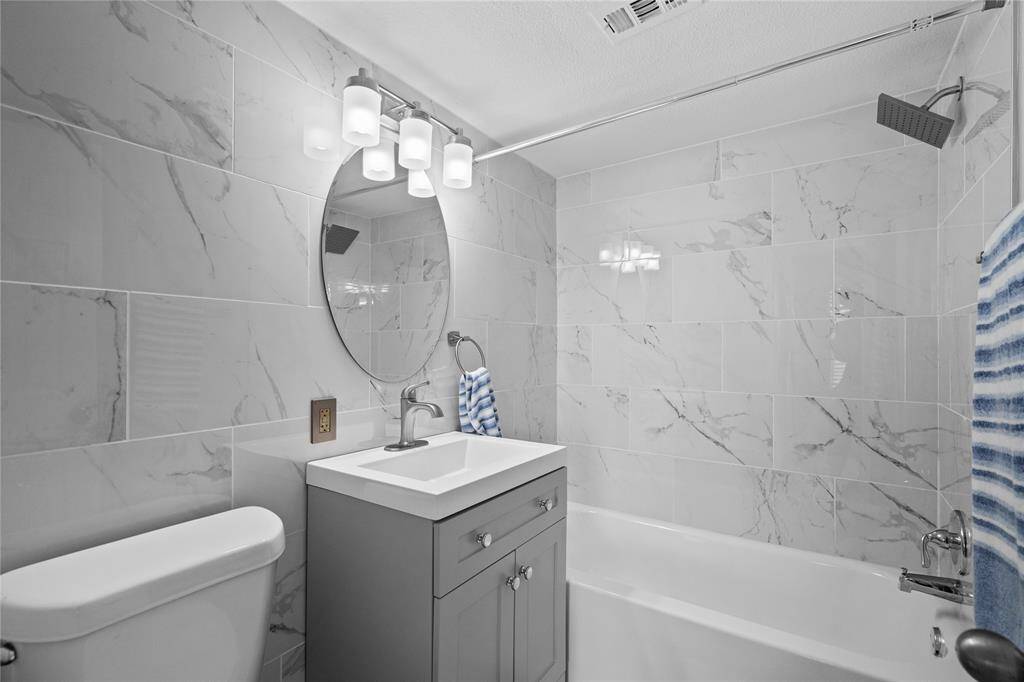 The master bathroom has quartz tile backsplash in bath/shower combo and wall behind sink cabinetry and toilet, waterfall showerhead, brushed nickle modern fixtures and finishes, and fresh paint!