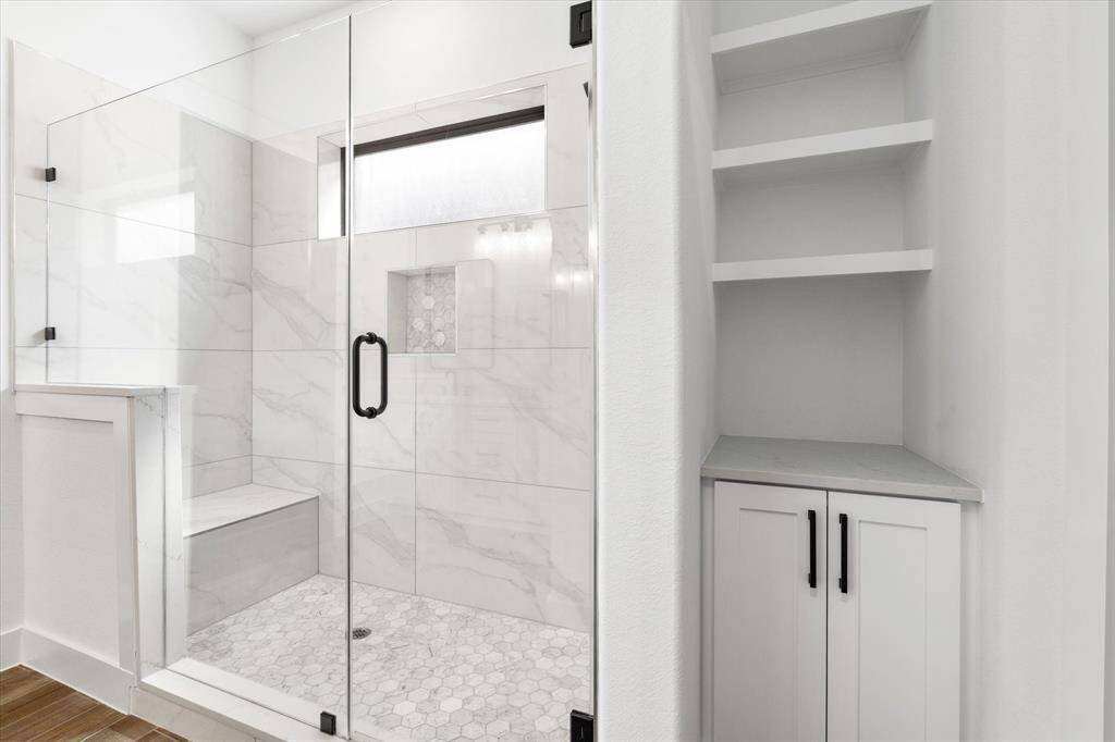 A spacious walk-in shower with a built in bench and soap niche. Additional built-in cabinets on the right for more storage.