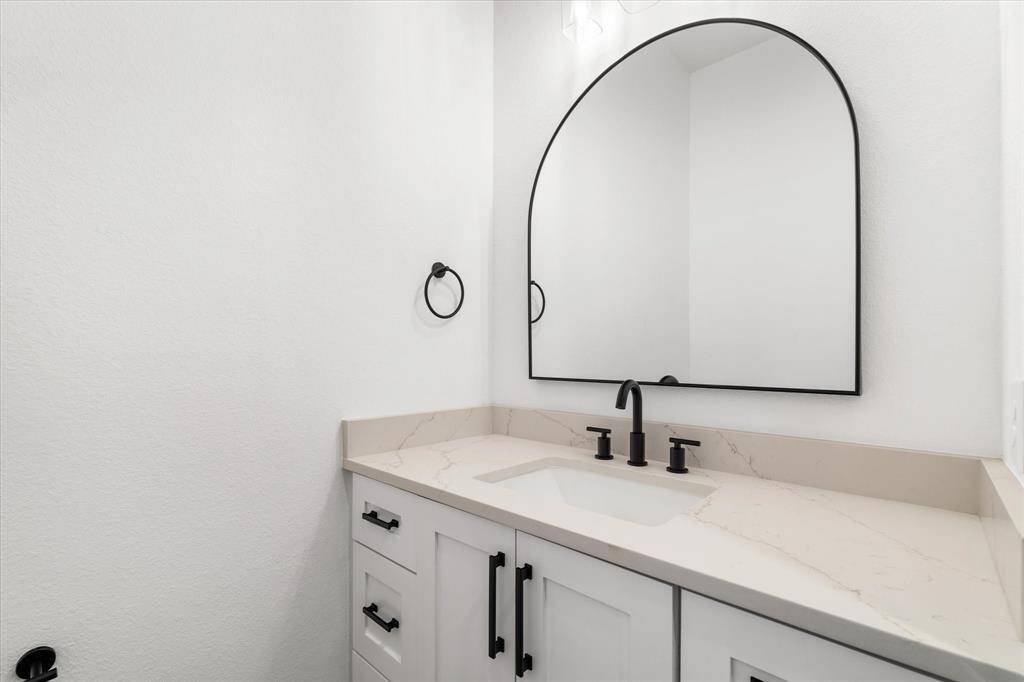 The half bath is enhanced with a sleek mirror, stylish cabinetry, and elegant quartz countertops, combining modern design with functional luxury.