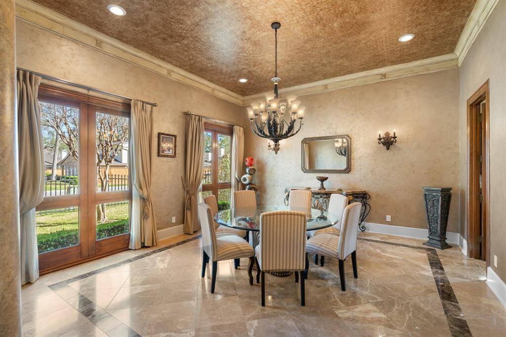 Elegant FORMAL DINING ROOM features a decorative tile ceiling detail and a stunning chandelier. Double crown molding and hand-painted textured walls add sophistication, while recessed can lighting provides a warm glow. Large windows with drapes offer views of the front yard. This spacious room is perfect for entertaining.