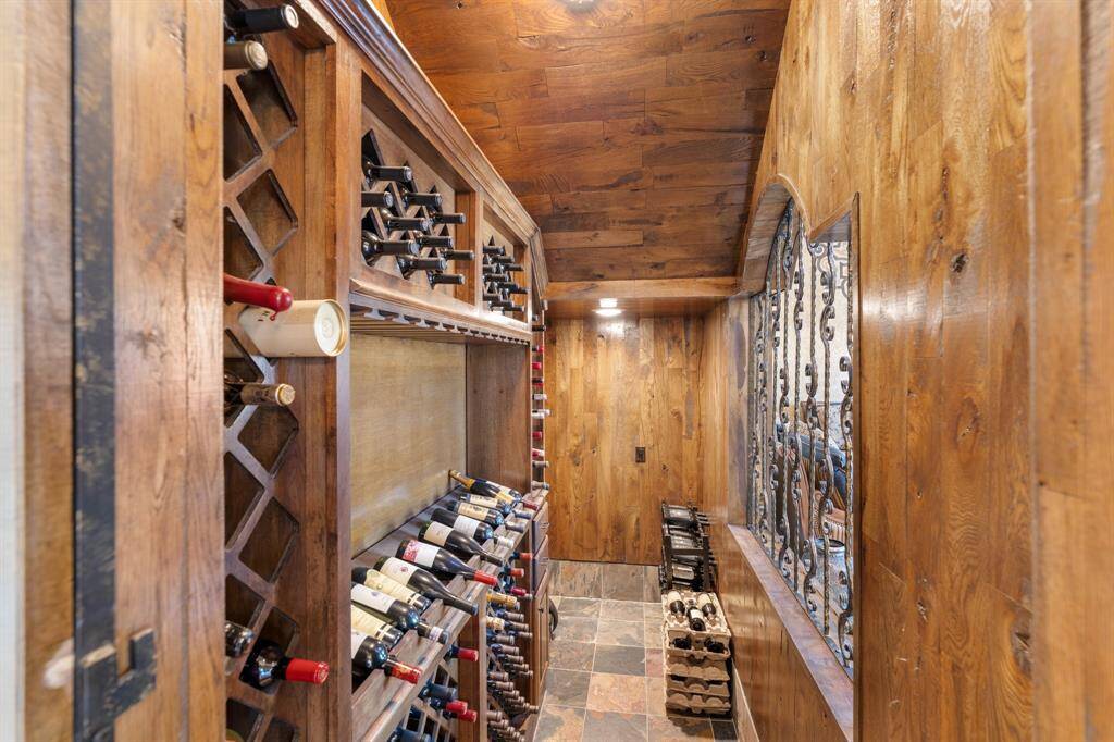 A peek into the gorgeous WINE ROOM featuring a flagstone floor and ample wine storage, perfect for any enthusiast. The space also includes a large storage closet and is enclosed by a decorative wrought iron door, adding a touch of elegance and style.