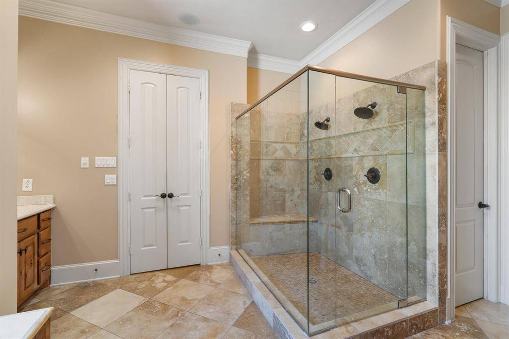 One last view of the primary bath showing the large walk-in shower with dual shower heads, bench seat, and glass surround. Not shown is an impressive vaulted ceiling, intricate ironwork, chandelier, and windows creating a stunning atmosphere.