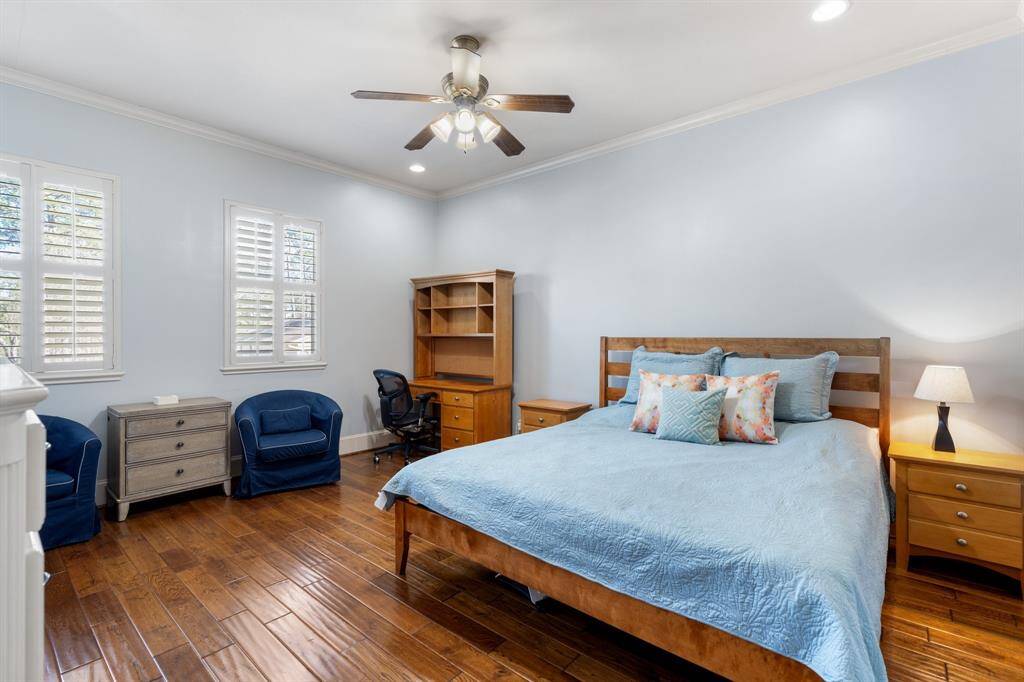 Located upstairs, this spacious SECONDARY BEDROOM #1 offers plenty of room for additional furniture. Featuring hardwood floors, plantation shutters, crown molding, recessed can lighting and a ceiling fan/light fixture. A built-in dresser and walk-in closet provide ample storage. Access to an ensuite Jack & Jill bathroom, with each bedroom having its own separate vanity space. Not shown is a built-in desk with storage and bookshelves, perfect for a study area.