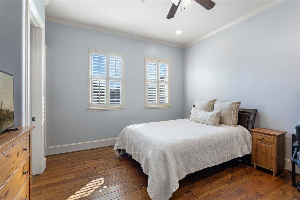 SECONDARY BEDROOM #2, located upstairs, features built-in bookshelves for added storage and style, hardwood floors, plantation shutters, crown molding, recessed can lighting and a ceiling fan/light fixture. This bedroom shares an ensuite Jack & Jill bathroom with Secondary Bedroom #1, each with its own separate vanity space. The bathroom also features a walk-in closet located in the vanity area.