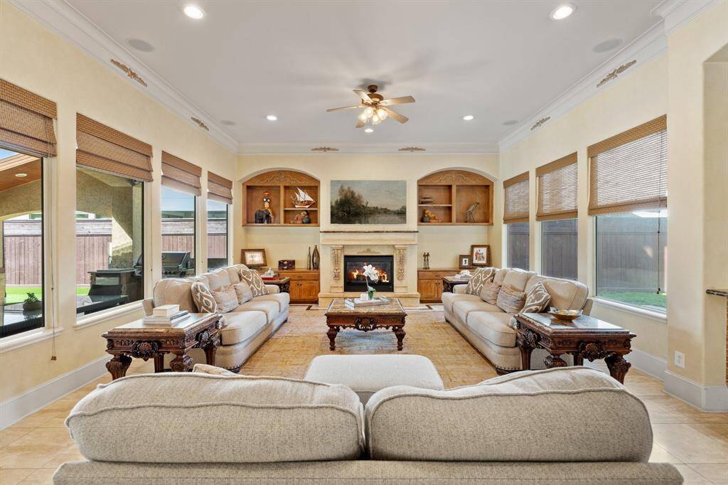 Fabulous light filled FAMILY ROOM offers ample space for versatile furniture arrangements. Two walls of windows bring in natural light with Hunter Douglas window treatments providing privacy and style. Book/display shelves and storage cabinets frame the fireplace. The gas fireplace, with intricate accent details and a marble mantle, serves as a stunning focal point. Dual ceiling fans and ceiling speakers enhance the comfort, and double crown molding and recessed lighting add to the room's elegance.