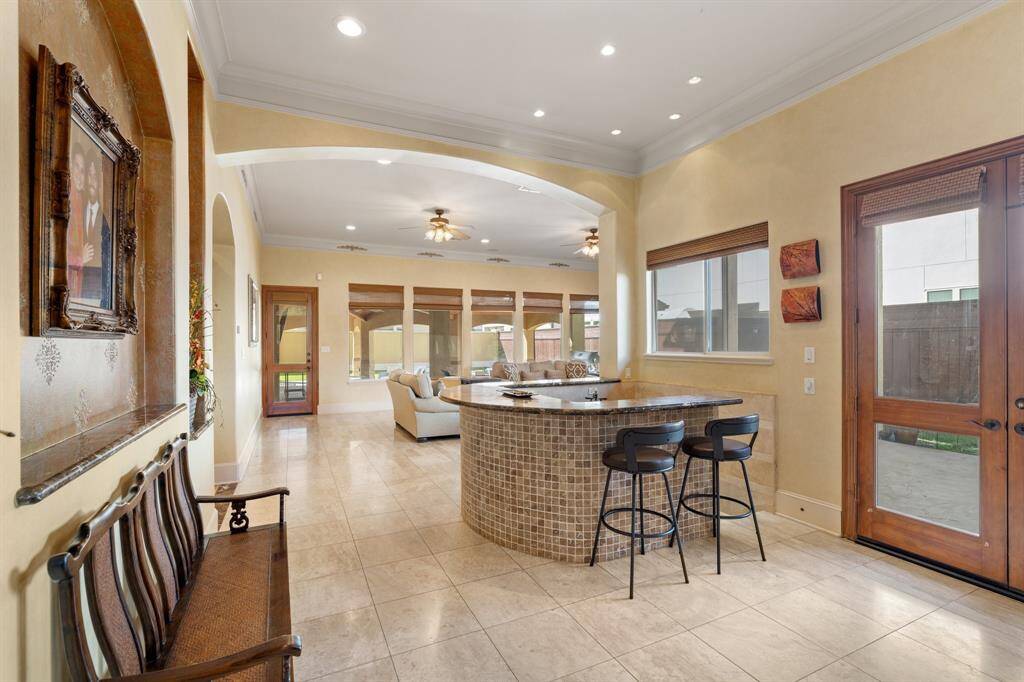 Leading into the family room is this stylish bar featuring a marble countertop and stone surround, complete with a bar sink. Centrally situated between the formals and family room.   The double glass doors with pull down shades on the right lead to a side yard patio space. This floor plan is ideal for entertaining friends and family.