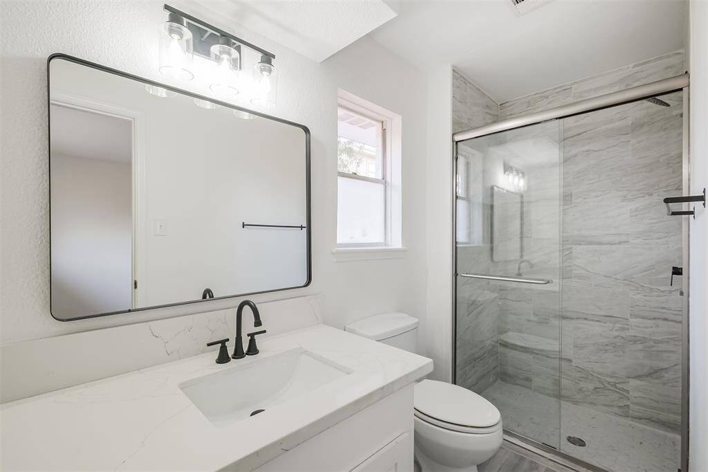 The primary bathroom features a new vanity, an elongated toilet, and a glass-enclosed walk-in shower, combining style and functionality.
